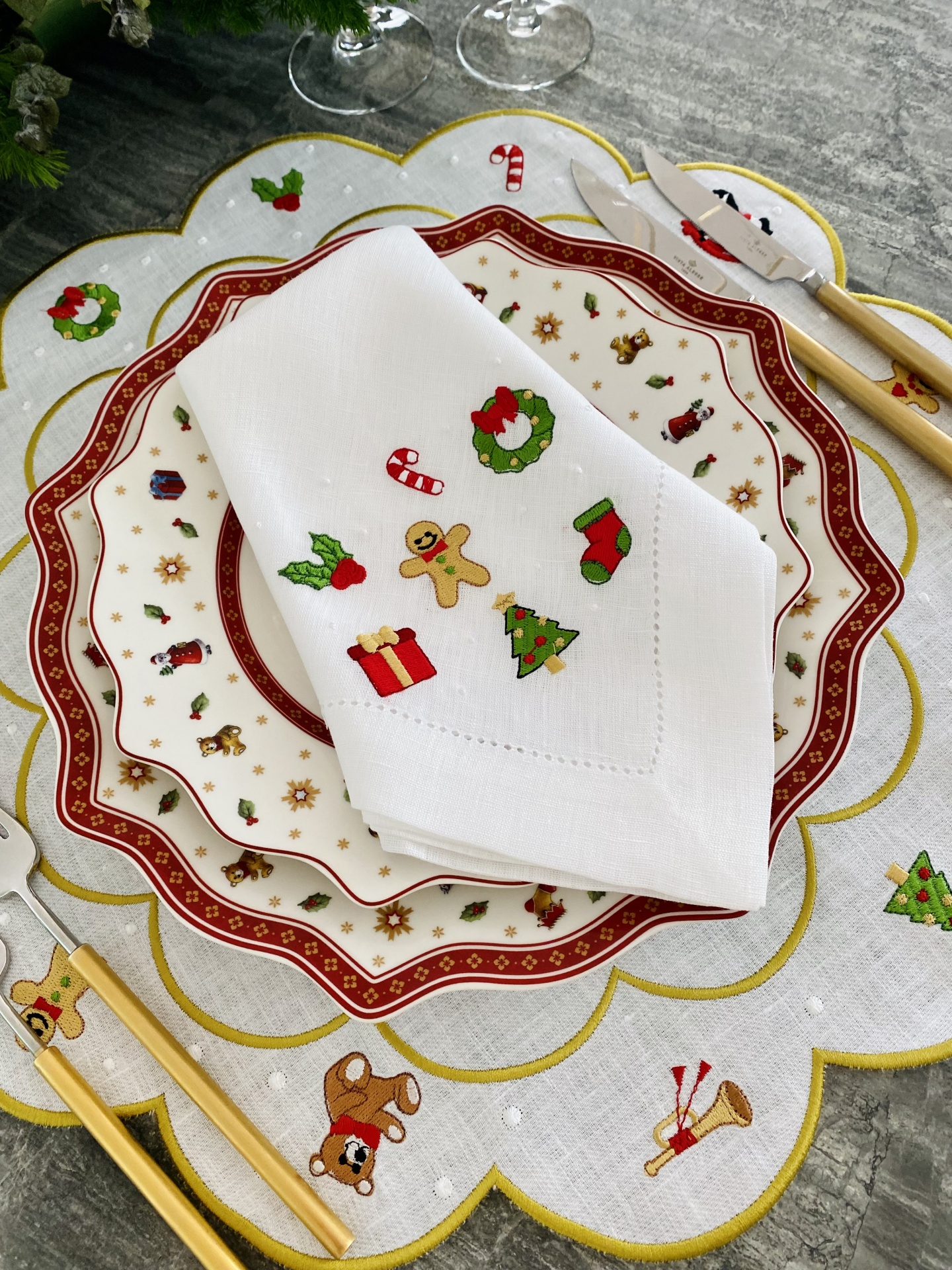 Conjunto de mesa com pratos, guardanapo natalício e talheres sobre toalha de mesa decorada