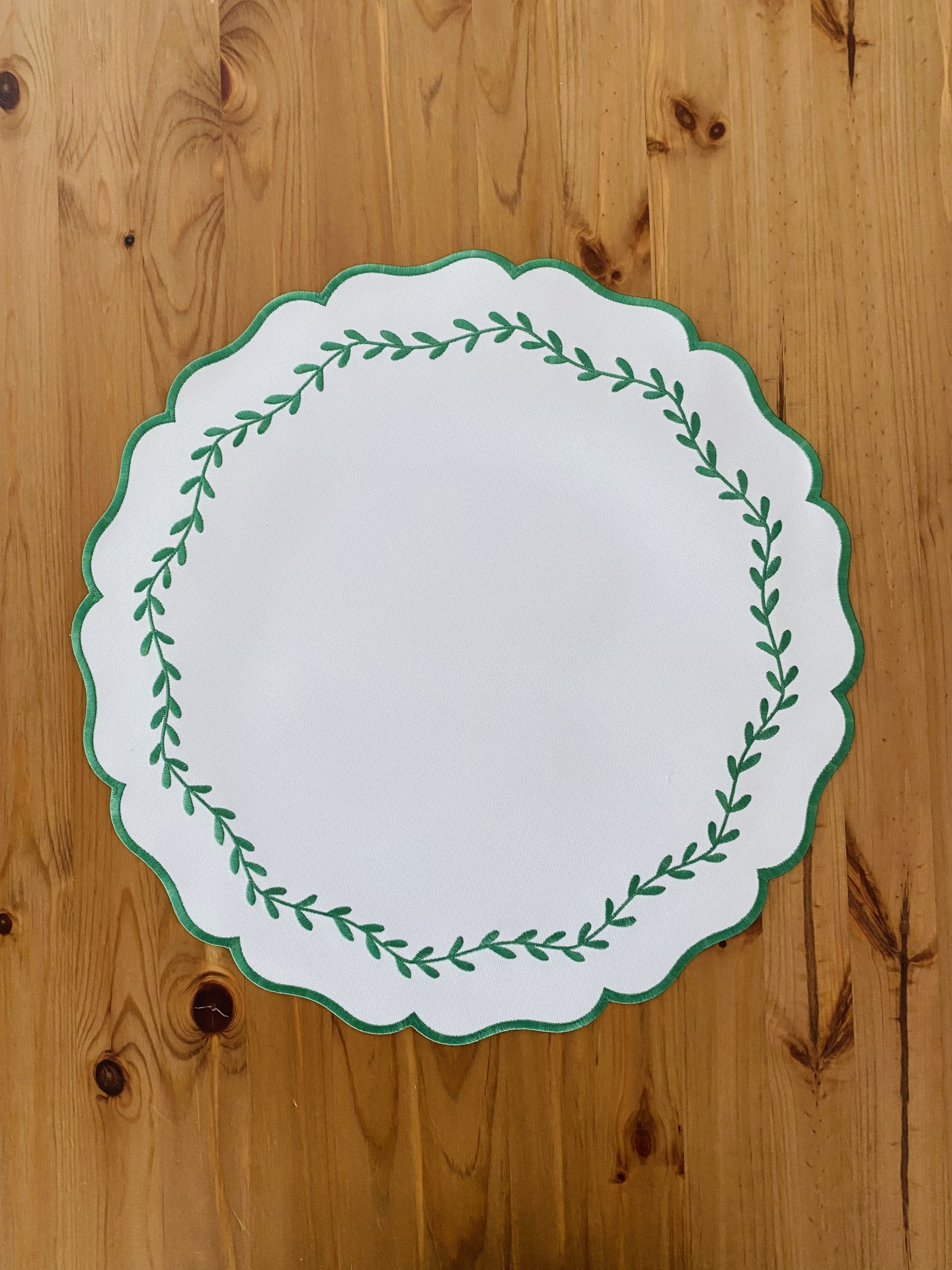 Porta-copo branco com borda verde e padrão de ramo verde sobre madeira clara