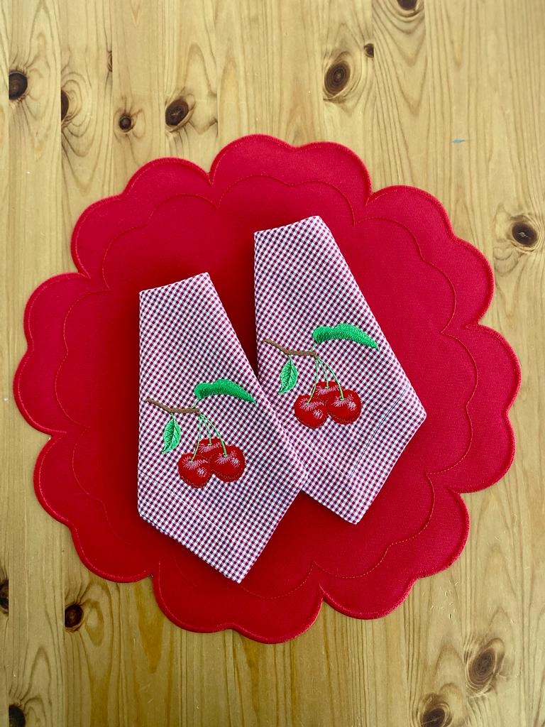 Panos de cozinha com estampa de cerejas sobre toalhete vermelho ondulado, em madeira clara