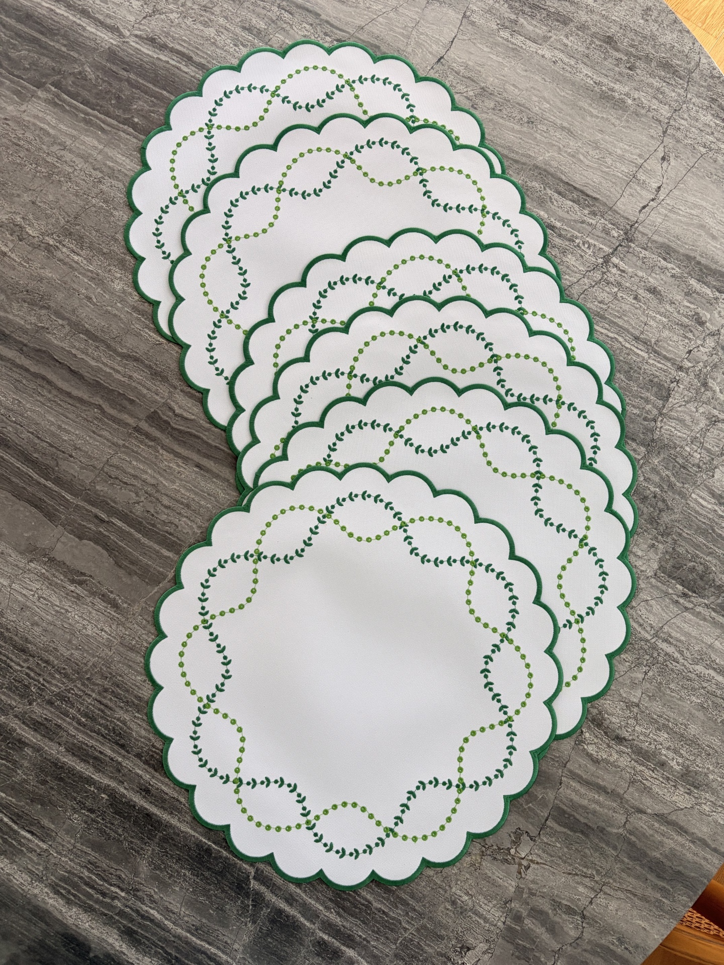Bases de mesa ovais brancas com bordas verdes e bordados em verde sobre superfície cinza.