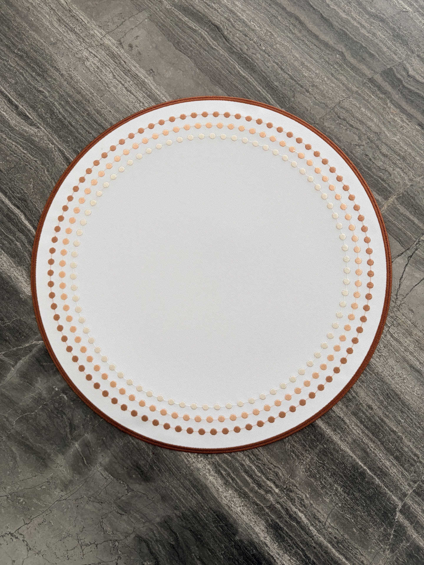 Tapete redondo branco com padrão de círculos castanhos sobre chão de pedra cinzenta
