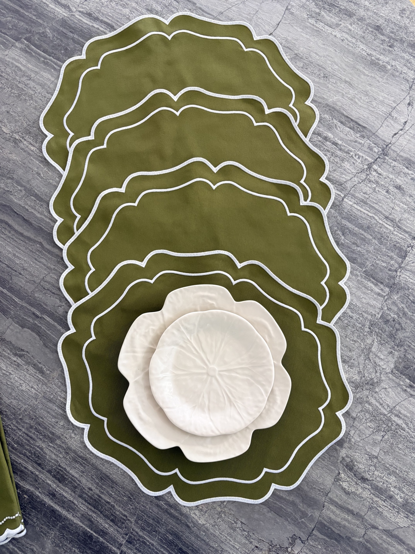 Individual de mesa verde-oliva com pratos brancos em forma de flor sobre pedra cinzenta
