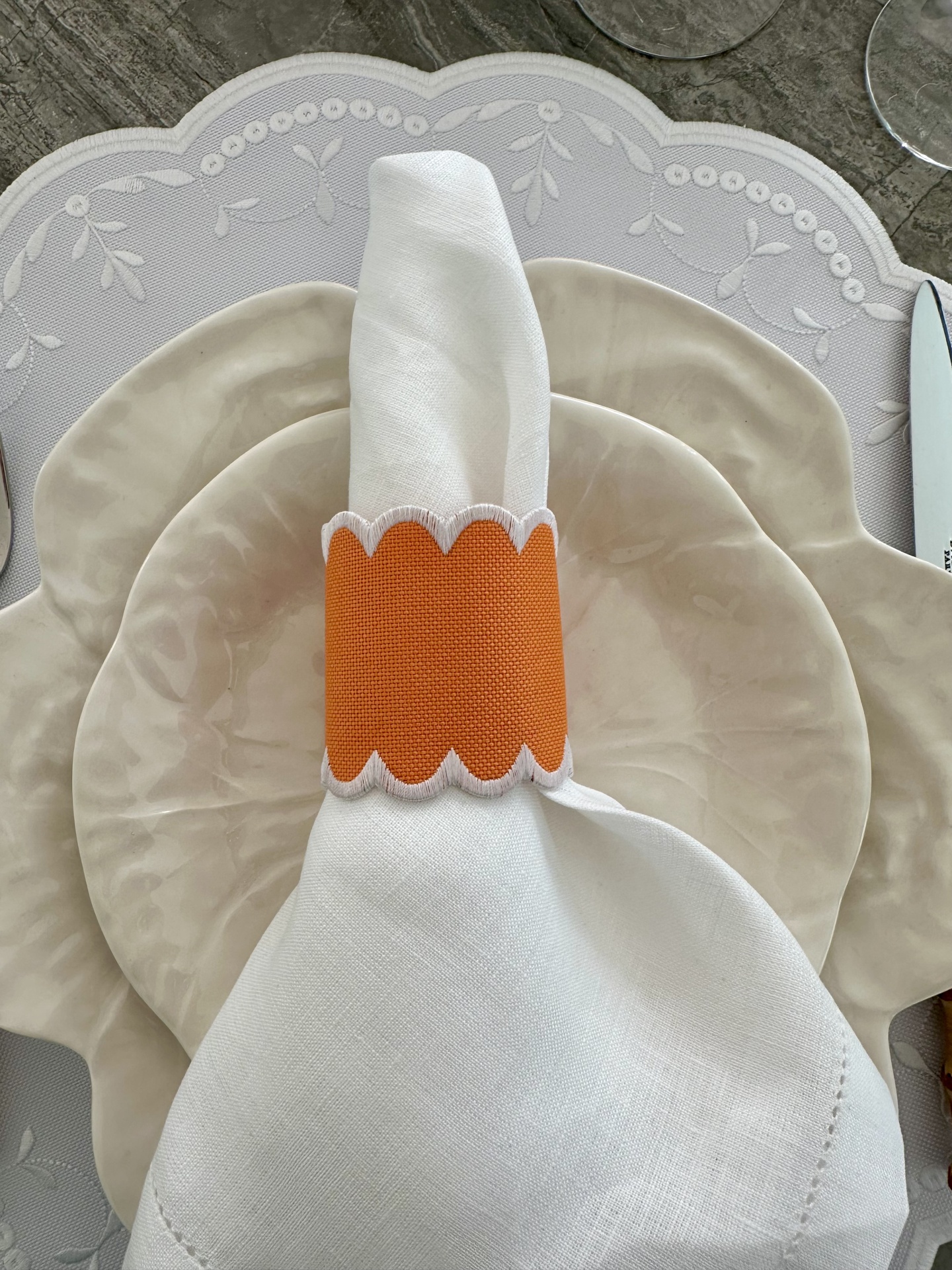 Pratos de cerâmica bege com guardanapo branco e anel de tecido laranja sobre toalha branca com padrão floral
