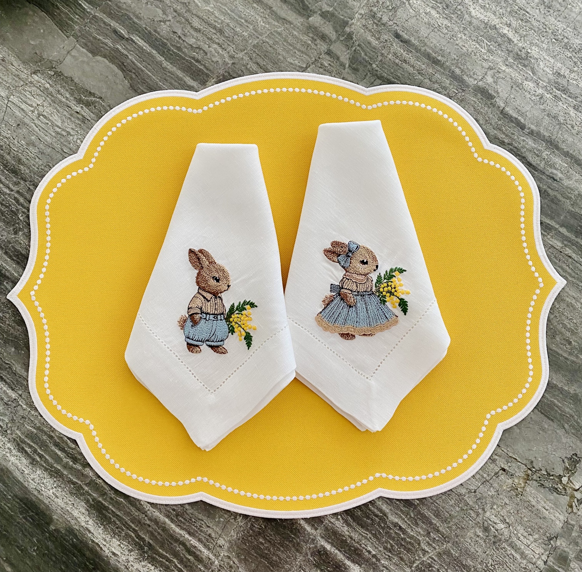 Dois guardanapos de pano com bordados de coelhos sobre sousplat amarelo