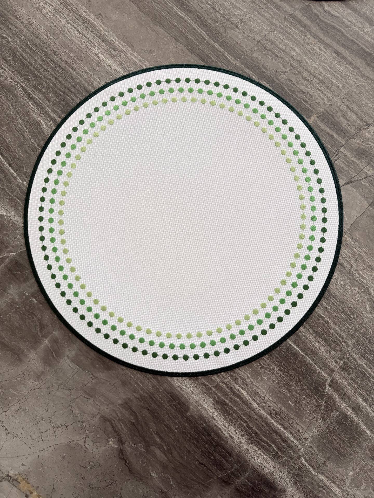Tapete redondo branco com pontos verdes em piso de pedra cinzenta