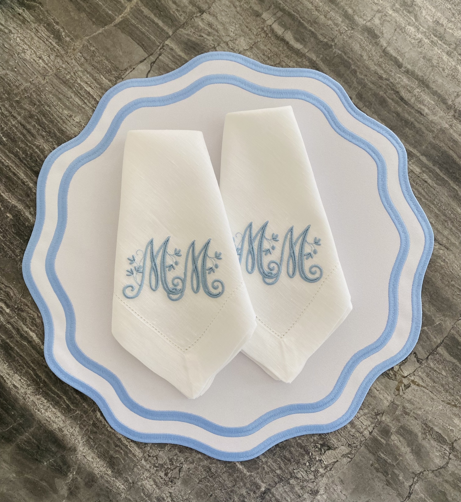 Guardanapos brancos bordados com letras azuis sobre prato branco com borda azul