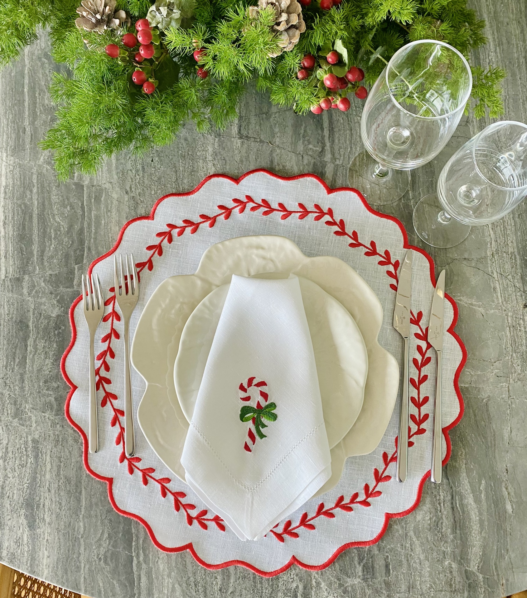 Conjunto de mesa natalício com prato branco, sousplat bordado vermelho, guardanapo com bengala de natal e talheres ao lado