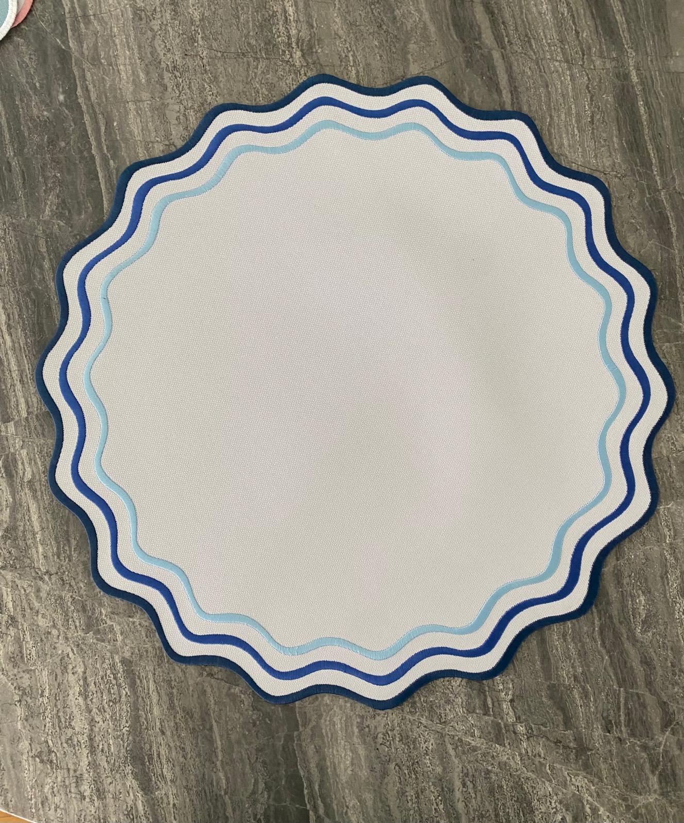 Tapete redondo azul com borda ondulada sobre piso de pedra cinzenta
