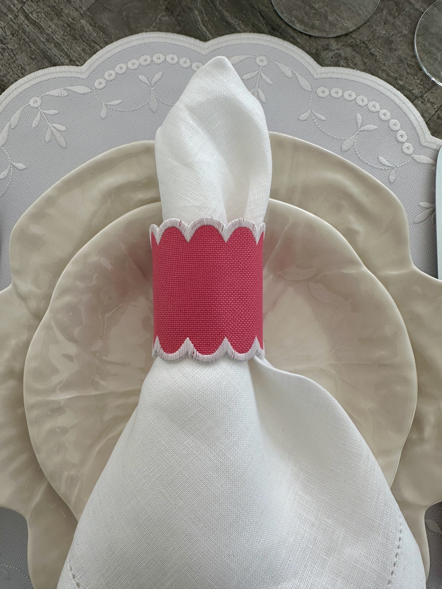 Conjunto de pratos e guardanapo com argola rosa sobre toalha branca bordada