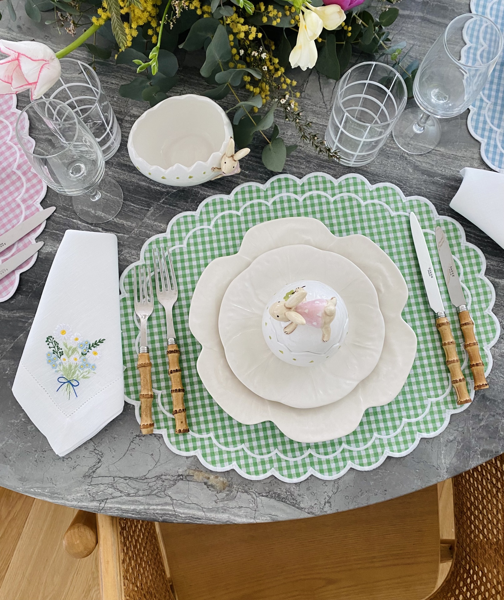 Mesa posta com prato xadrez verde, pratos brancos, talheres com cabos de bambu e guardanapo bordado