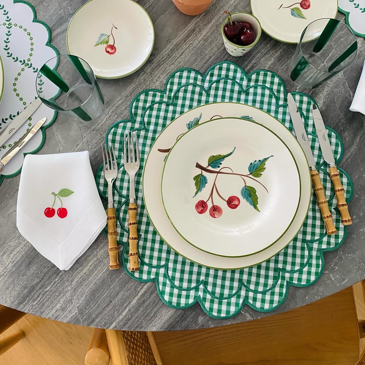 Mesa posta com pratos e talheres decorados com cerejas e padrão vichy verde e branco