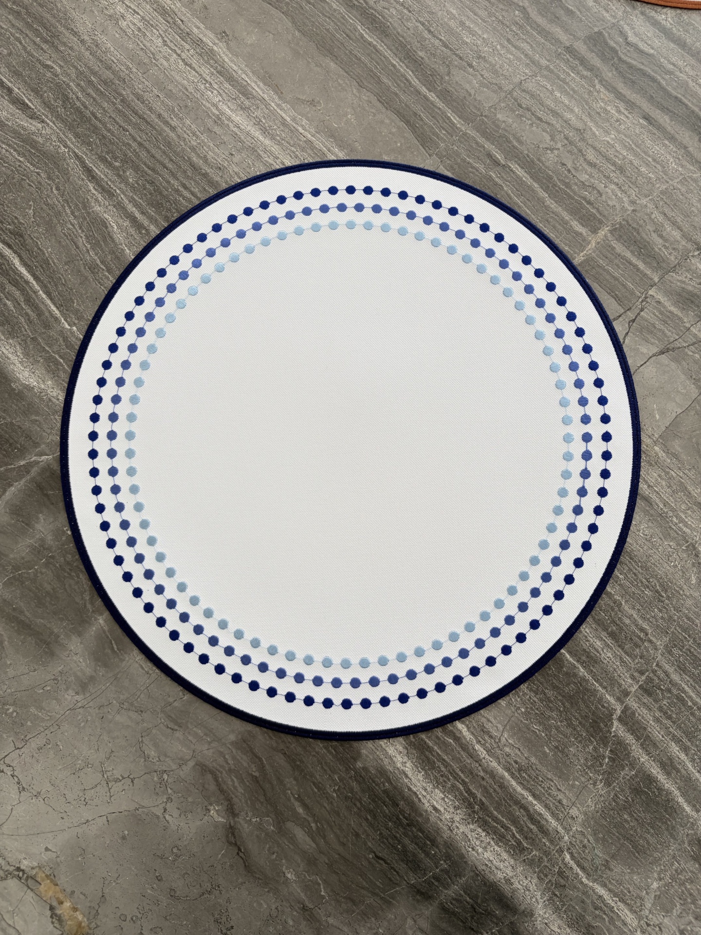 Tapete redondo branco com padrão de pontos azuis sobre chão de mármore cinza