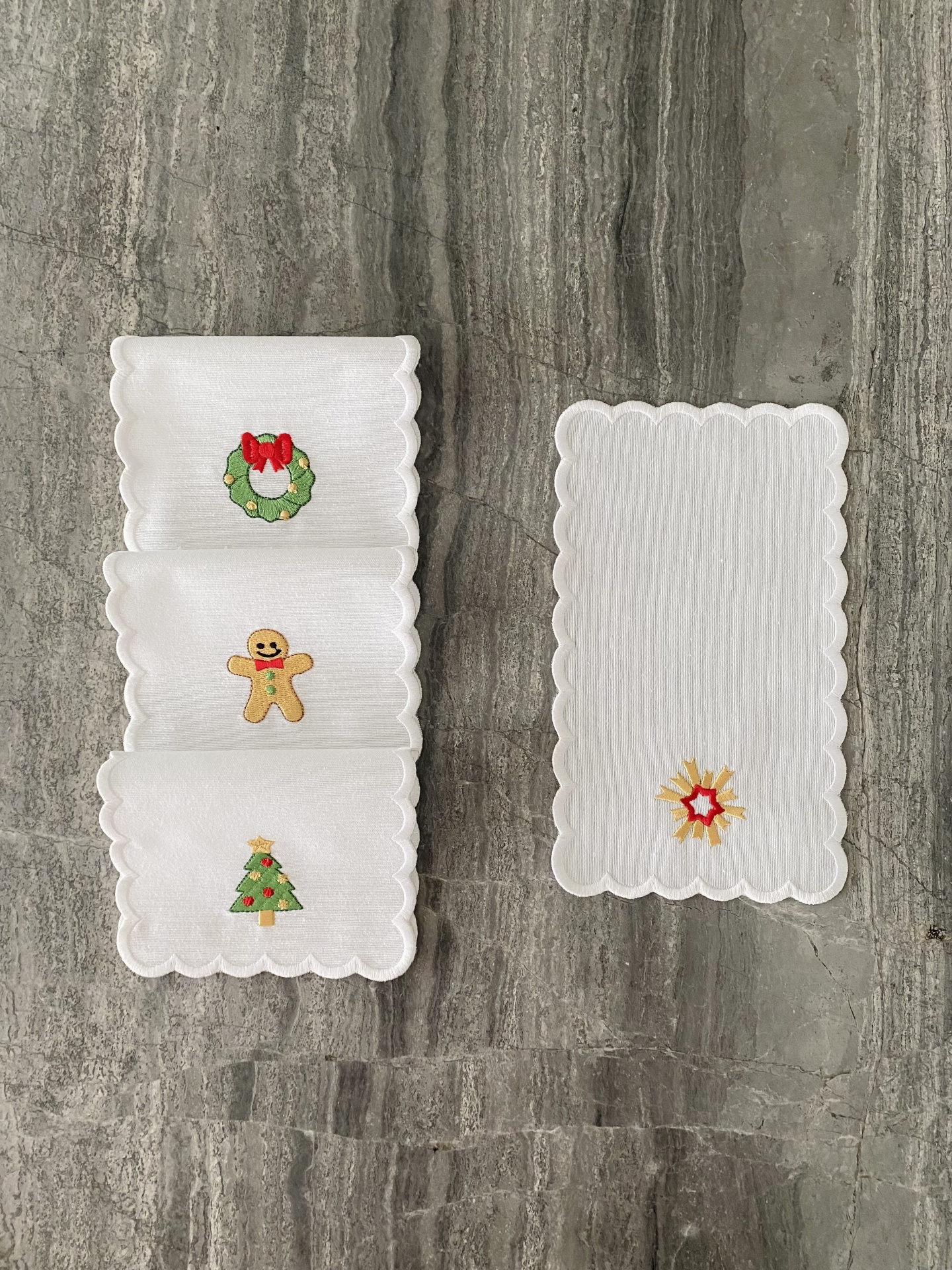 Guardanapos brancos com bordados de Natal e bordas onduladas numa superfície cinzenta