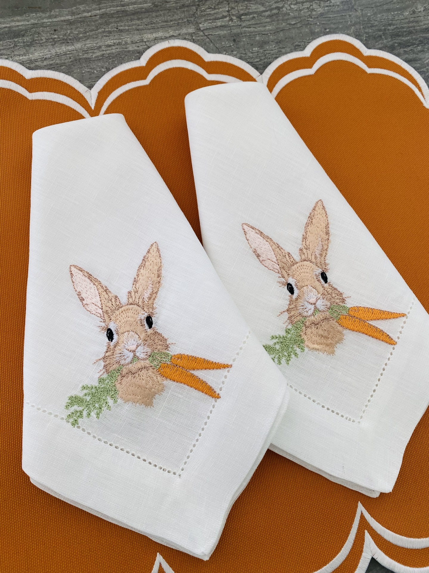 Toalhas de linho branco com bordado de coelho e cenouras, em cima de suportes castanhos com contorno branco