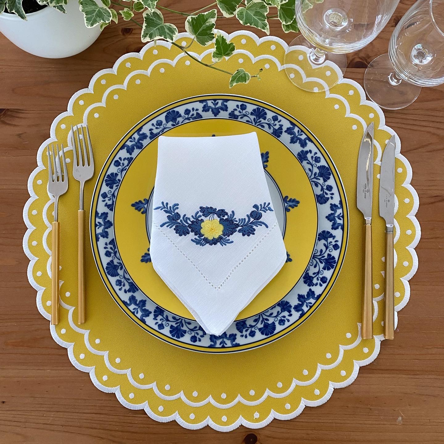 Conjunto de louça amarelo e branco com padrão azul e talheres amarelos numa mesa de madeira