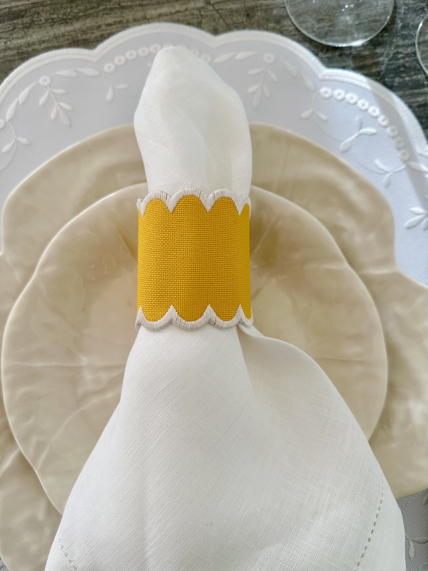 Guardanapo branco com anel amarelo sobre pratos bege e branco num fundo de madeira cinzenta