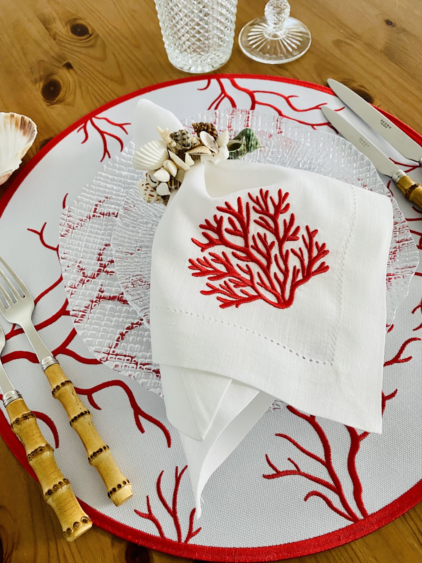 Conjunto de mesa com decoração vermelha de coral e talheres com cabos de bambu numa mesa de madeira