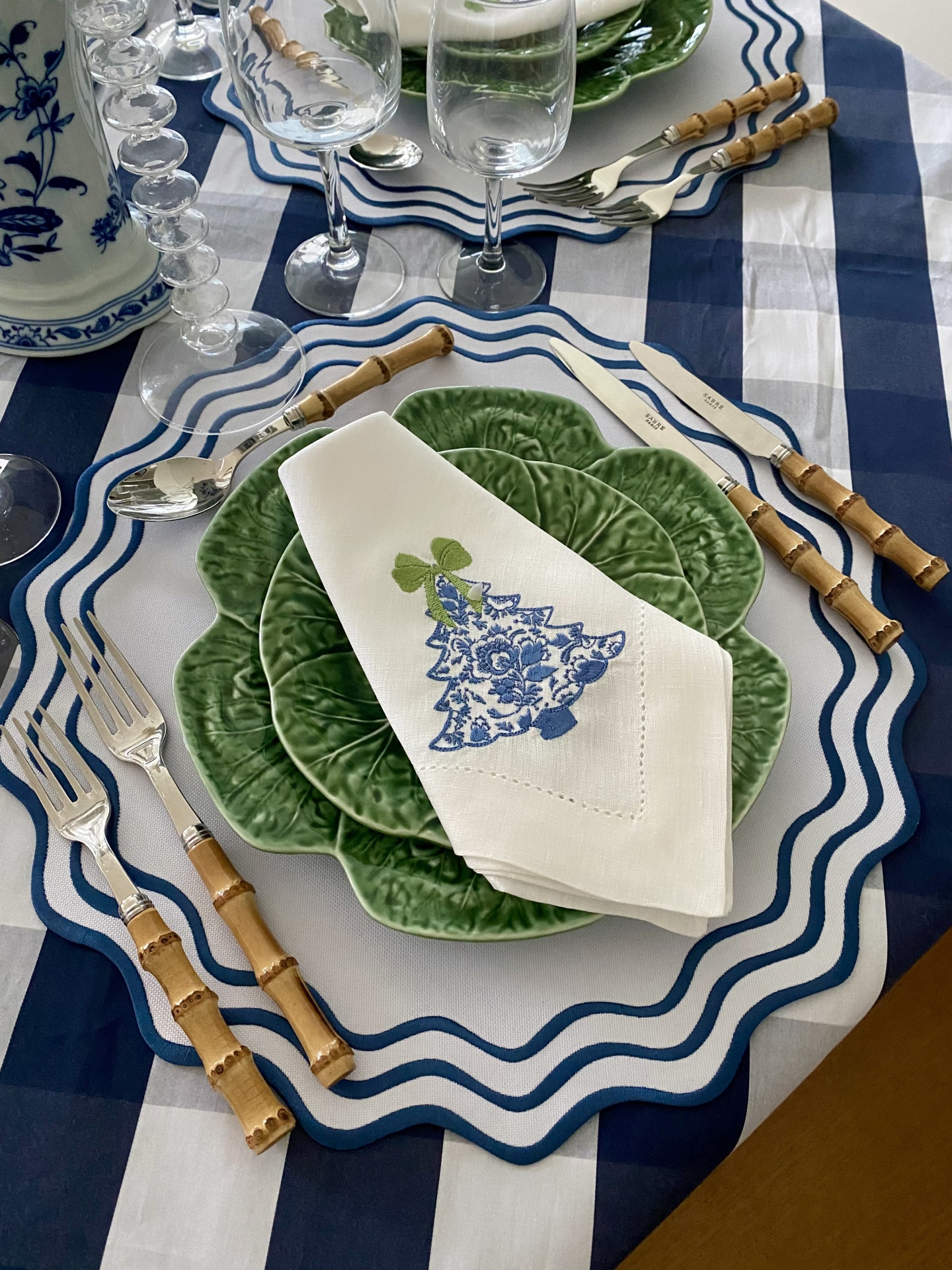 Mesa posta com pratos verdes texturizados, guardanapo bordado, talheres com cabo de bambu e toalha xadrez azul