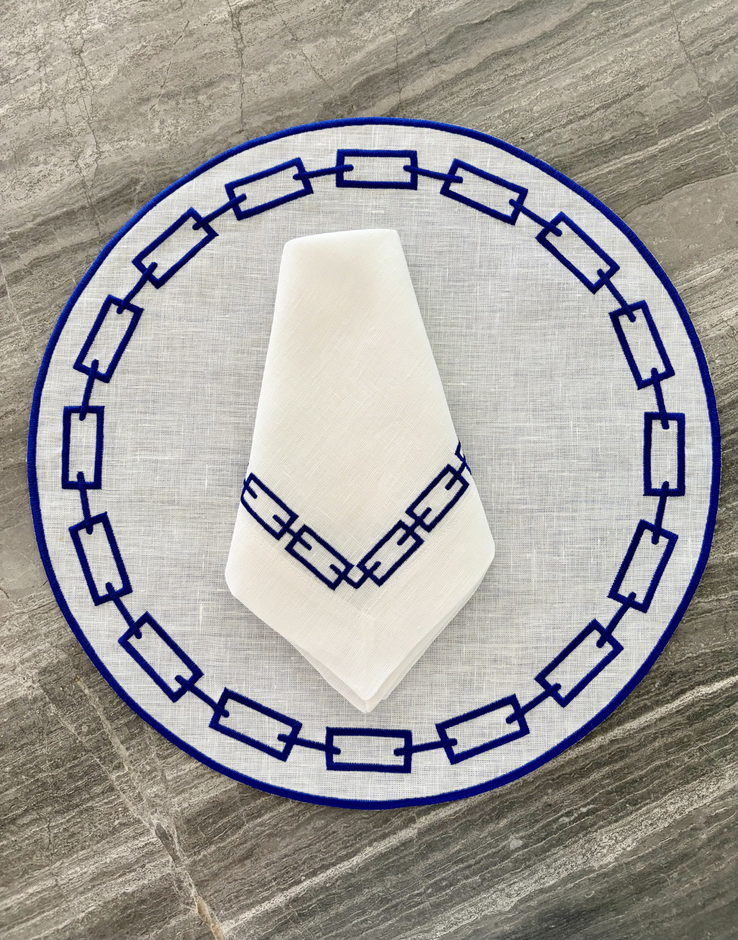Jogo de mesa redondo com toalha branca e padrão azul geométrico sobre pedra cinza