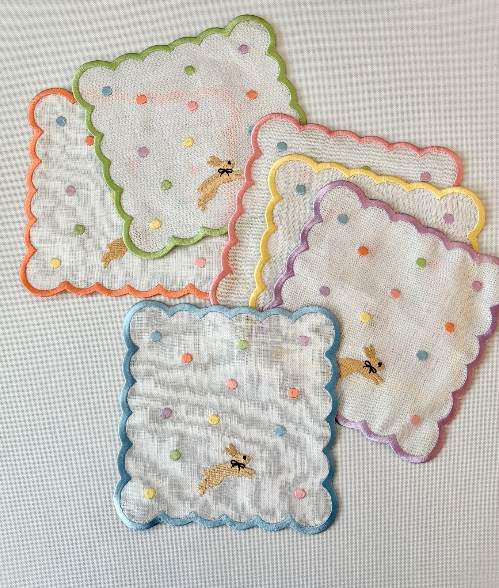 Conjunto de seis lenços brancos em linho com bordas coloridas e bordados de bolinhas e coelhos.