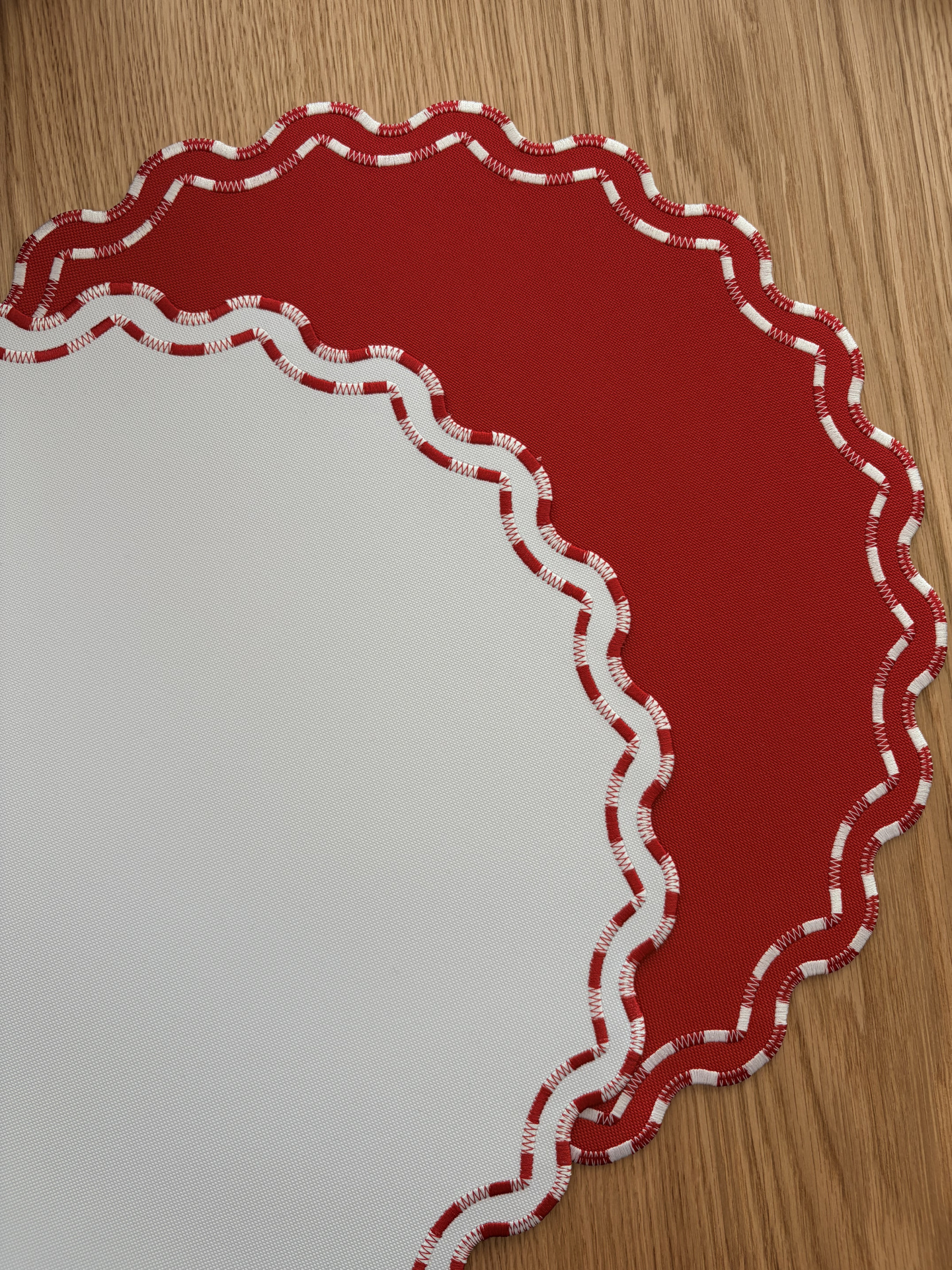 Dois jogos americanos de tecido vermelho e branco com bordas onduladas sobre madeira clara.