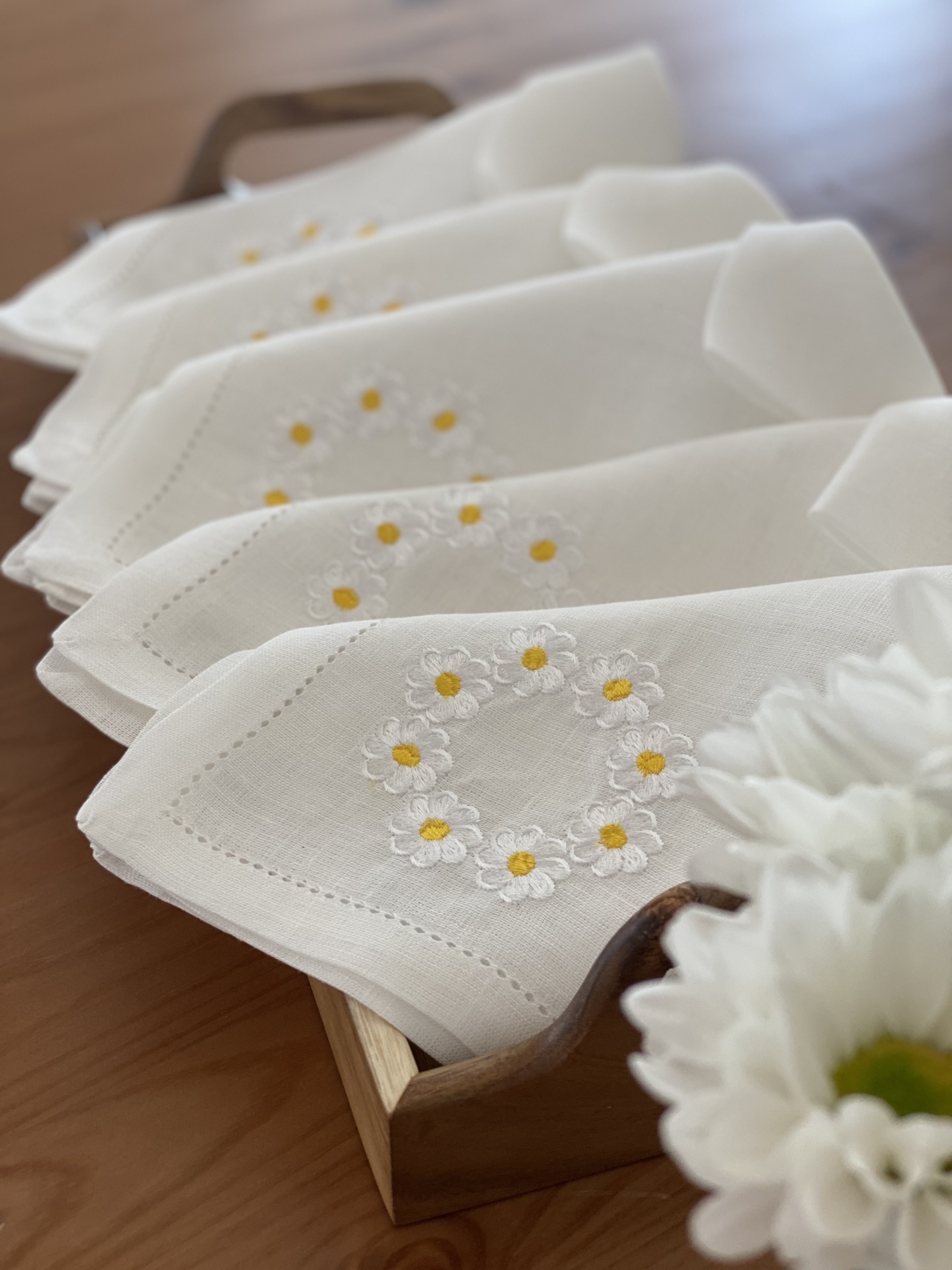Toalhas brancas bordadas com flores amarelas e brancas numa caixa de madeira.