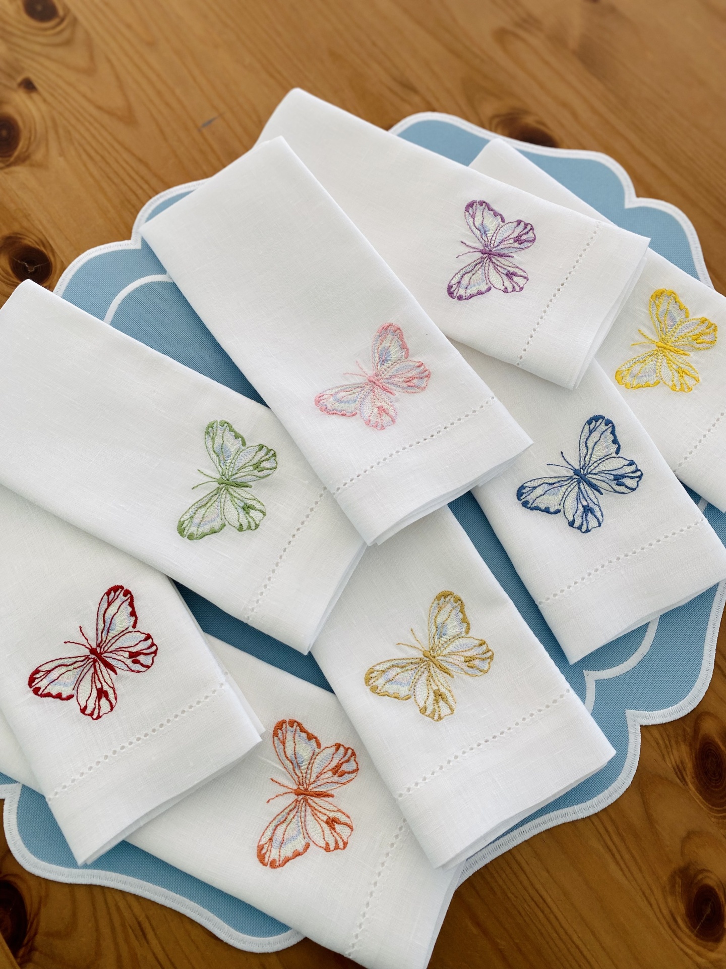 Guardanapos brancos com bordados coloridos de borboletas em prato azul sobre mesa de madeira