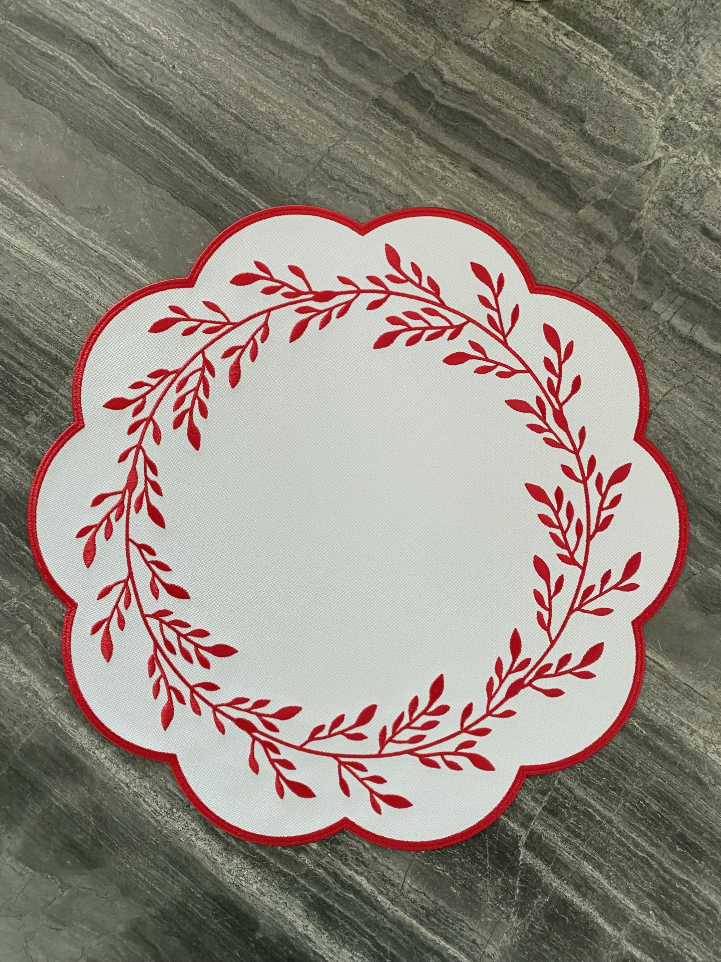 Individual de mesa branco com ramos vermelhos e borda em pétalas sobre pedra cinzenta