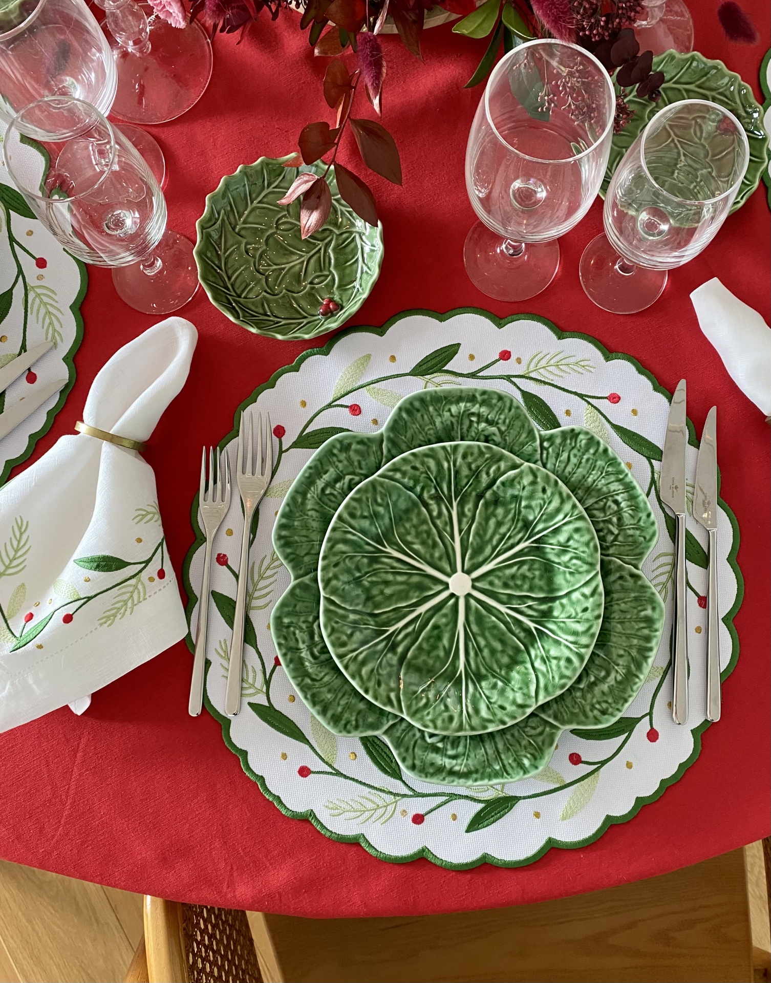 Conjunto de loiça verde com padrão de folhas e toalha vermelha.