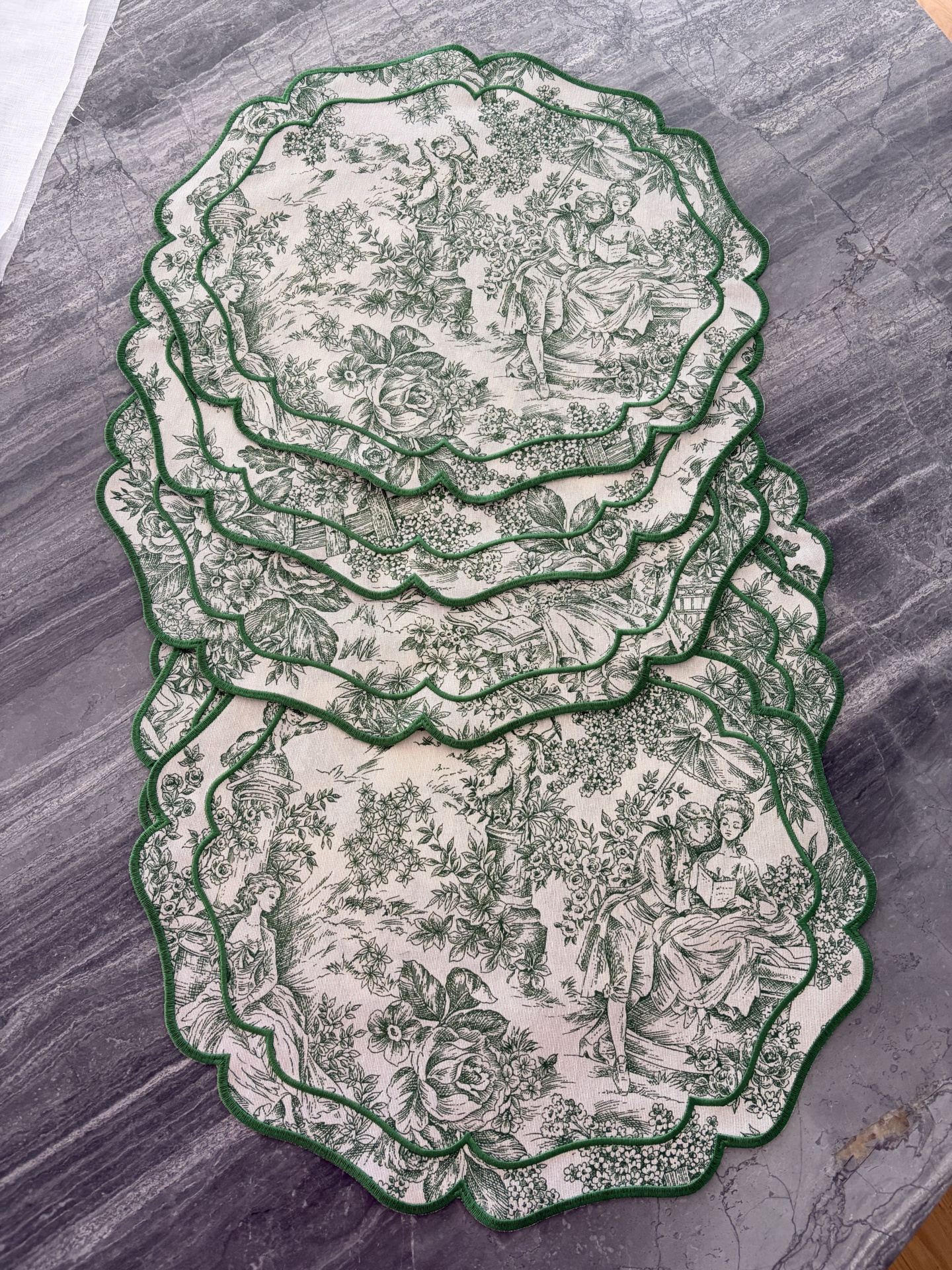Guardanapos de tecido vintage com padrão verde e branco e bordas onduladas verdes numa mesa cinza.