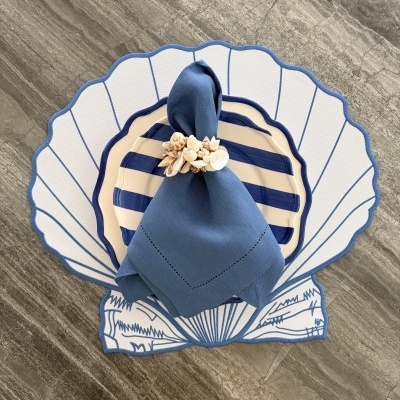 Conjunto de pratos com guardanapo azul e suporte em formato de concha em superfície cinza