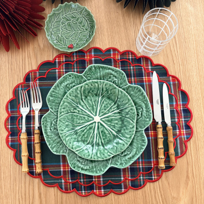 Conjunto de mesa com pratos verdes em forma de folha, talheres com cabo em bambu, toalhetes xadrez e copo transparente.