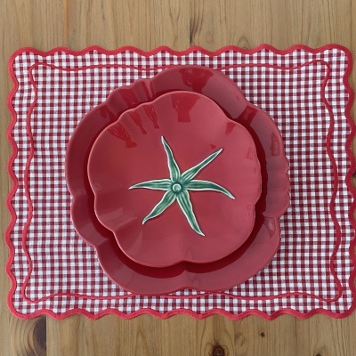 Dois pratos vermelhos em forma de tomate sobre jogo americano vermelho e branco, em mesa de madeira