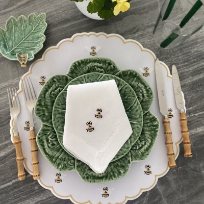 Conjunto de loiça com prato branco decorado com abelhas, prato verde tipo folha, guardanapo branco com abelhas e talheres de cabo madeira