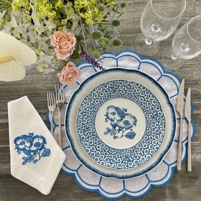 Mesa posta com prato azul e branco, guardanapo bordado, talheres e flores