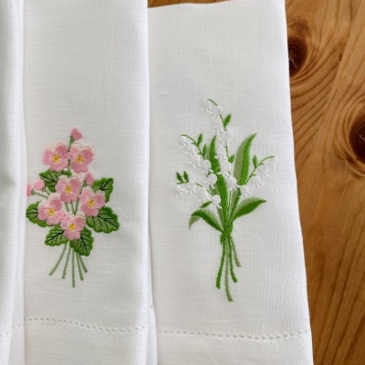 Guardanapos brancos com bordados florais rosa e branco sobre mesa de madeira.