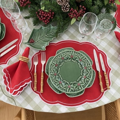 Conjunto de loiça de cerâmica verde com padrão de folhas e bagas vermelhas numa mesa com individual vermelho, talheres de cabo de madeira e guardanapo vermelho