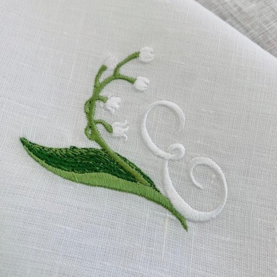 Pano branco com bordado de ramo verde com flores brancas e letra E em branco