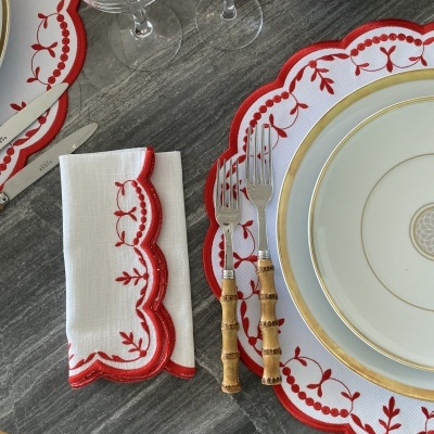 Conjunto de jantar com guardanapo bordado vermelho, pratos brancos com dourado e talheres com cabos de madeira