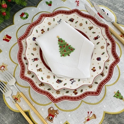 Conjunto de loiça e guardanapo com padrões natalícios em cima de individual cinzento bordado com motivos de Natal