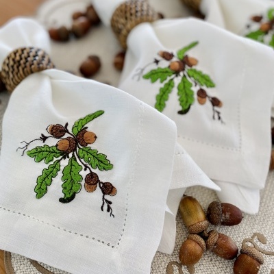 Guardanapos bordados com ramos de carvalho e bolotas com argolas trançadas sobre suporte decorativo