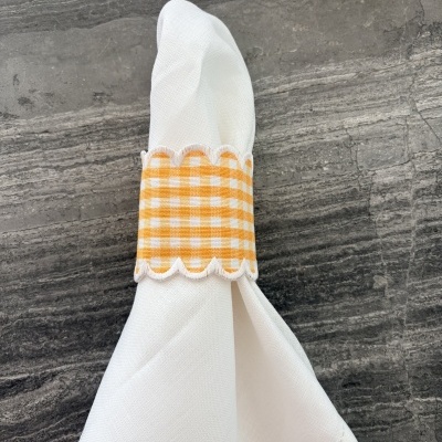 Guardanapo branco com argola xadrez amarelo e branco numa superfície cinza escura