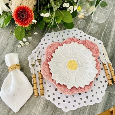 Mesa posta com pratos em forma de flor, talheres com cabo de madeira, guardanapo branco e flores coloridas