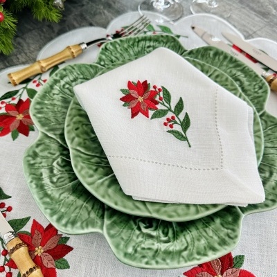 Louça verde com textura, guardanapo branco bordado com flor vermelha, talheres de madeira e prata, toalha com motivos natalícios.