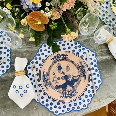 mesa decorada com prato cerâmico azul e branco, guardanapo branco, copos de vidro e arranjo floral colorido