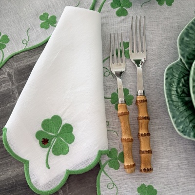 Mesa posta com guardanapo branco e bordado verde de trevo, garfos com cabo de bambu, prato verde em cerâmica e toalha com padrão de trevo