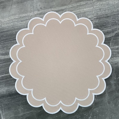 Tapete redondo bege claro com contorno branco em padrão ondulado sobre chão de pedra cinzenta