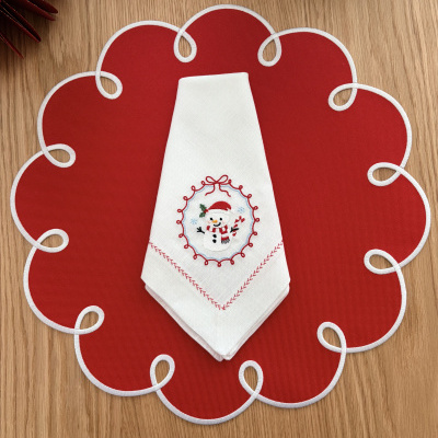 Guardanapo branco bordado com boneco de neve em jogo americano vermelho com contorno branco em mesa de madeira.