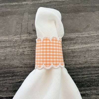 Guardanapo branco com argola laranja aos quadrados numa superfície cinzenta