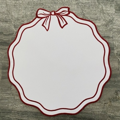 Individual de mesa branco com bordas vermelhas e desenho de laço, sobre superfície de pedra cinzenta